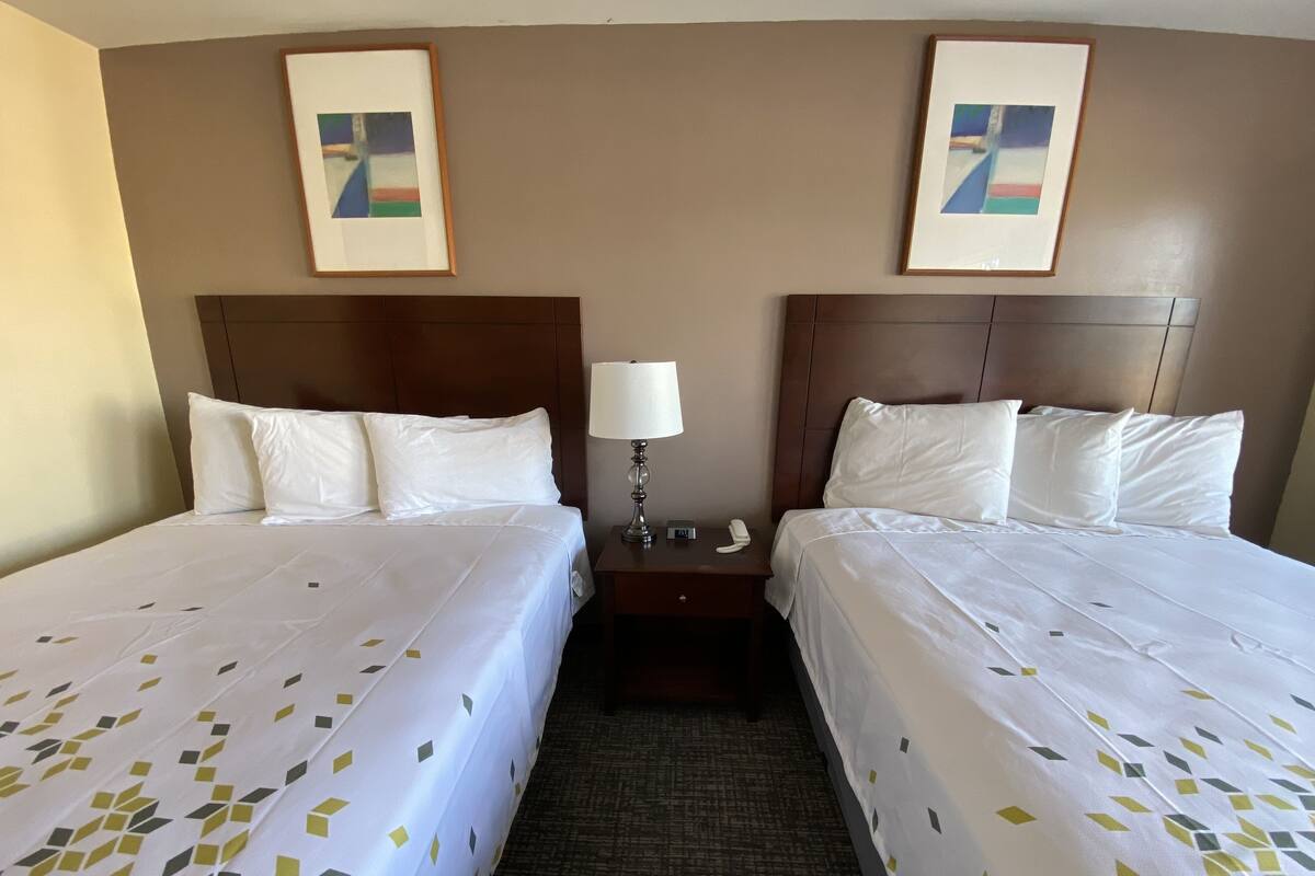 A hotel room with two beds, a nightstand with a lamp, and two framed pictures on the wall.