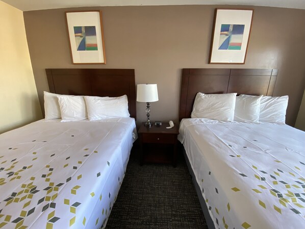 A hotel room with two beds, a nightstand with a lamp, and two framed pictures on the wall.
