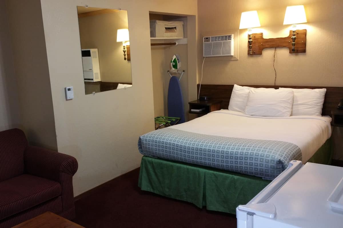 A hotel room with a bed, a green skirted table, a red striped sofa, a mirror, a wall-mounted heater, and a wall-mounted lamp.