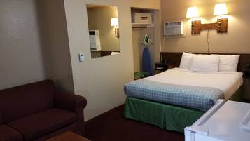 Une chambre d’hôtel avec un lit, une table verte à jupe, un canapé rouge à rayures, un miroir, un radiateur fixé au mur et une lampe fixée au mur.