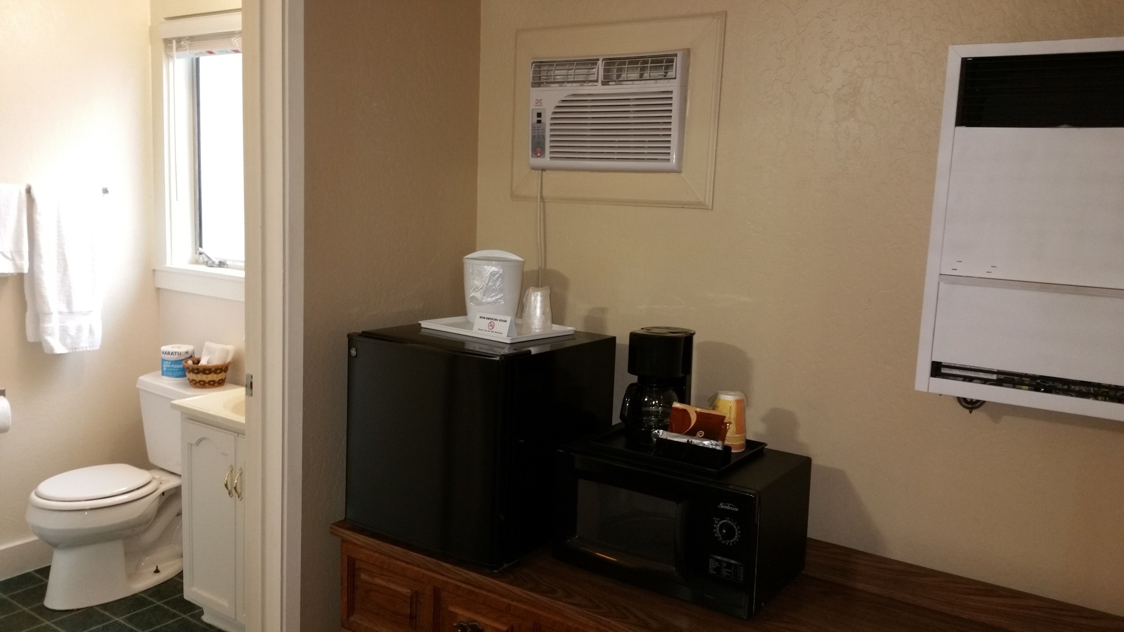 A bathroom with a toilet, a sink, a coffee maker, and a microwave on a wooden cabinet.