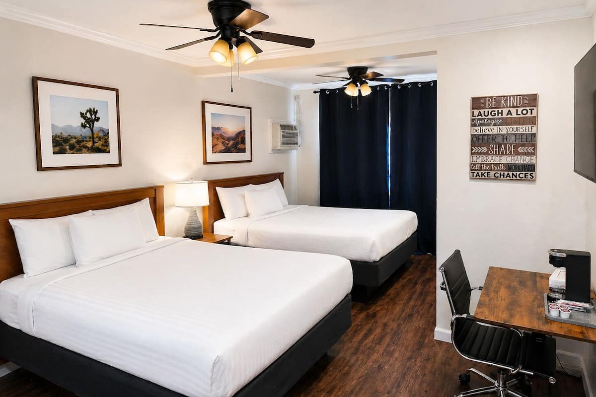 A hotel room with two beds, a desk with a chair, a ceiling fan, and motivational wall art.