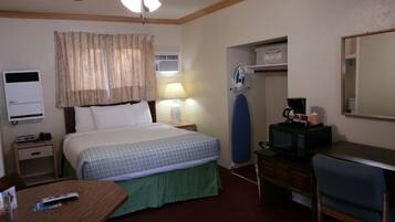 Habitación de hotel con cama, lámpara de noche, equipo de aire acondicionado, microondas y escritorio con silla.