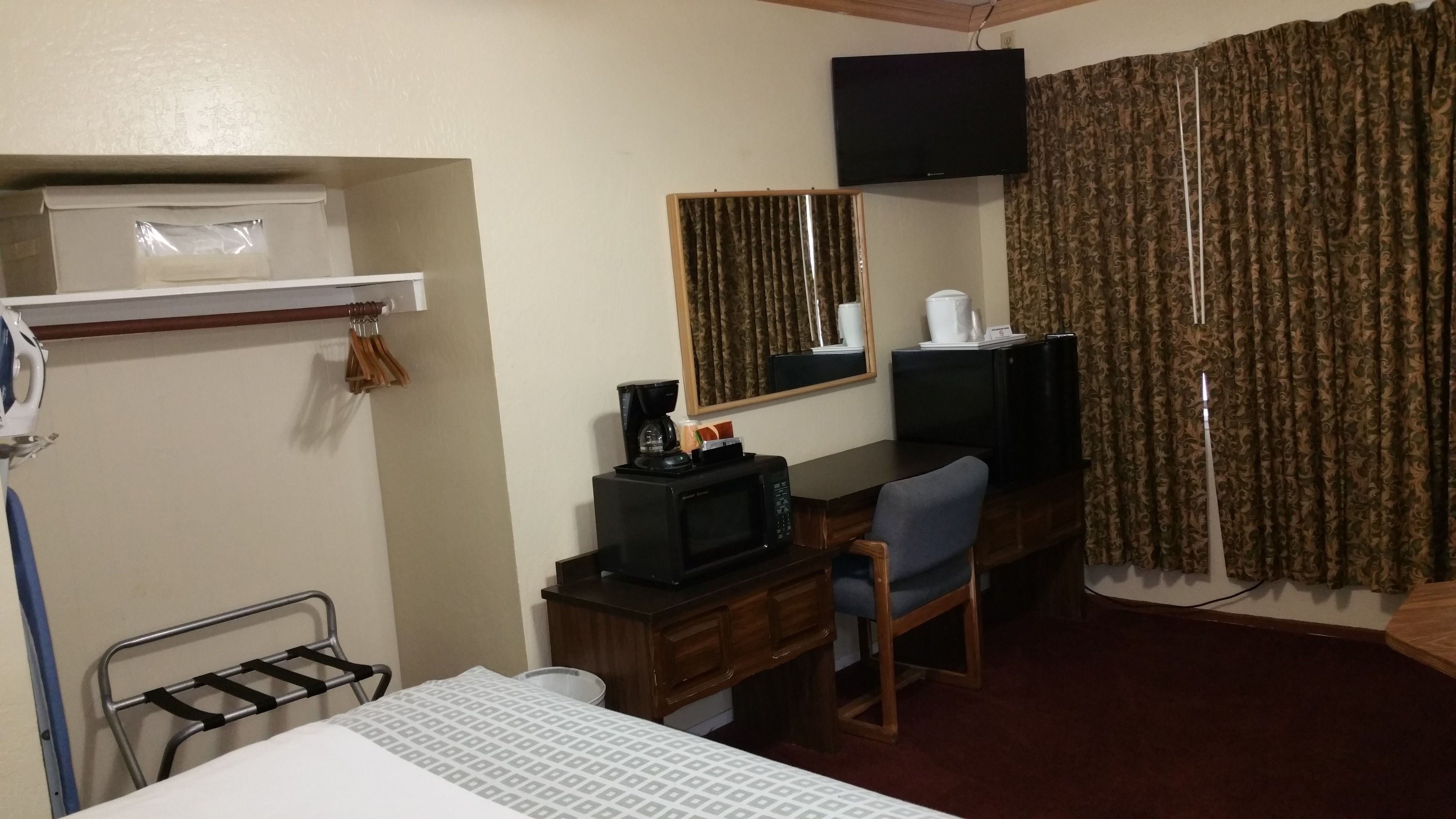Una habitación de hotel con cama, escritorio, silla, televisión, cafetera y espejo.