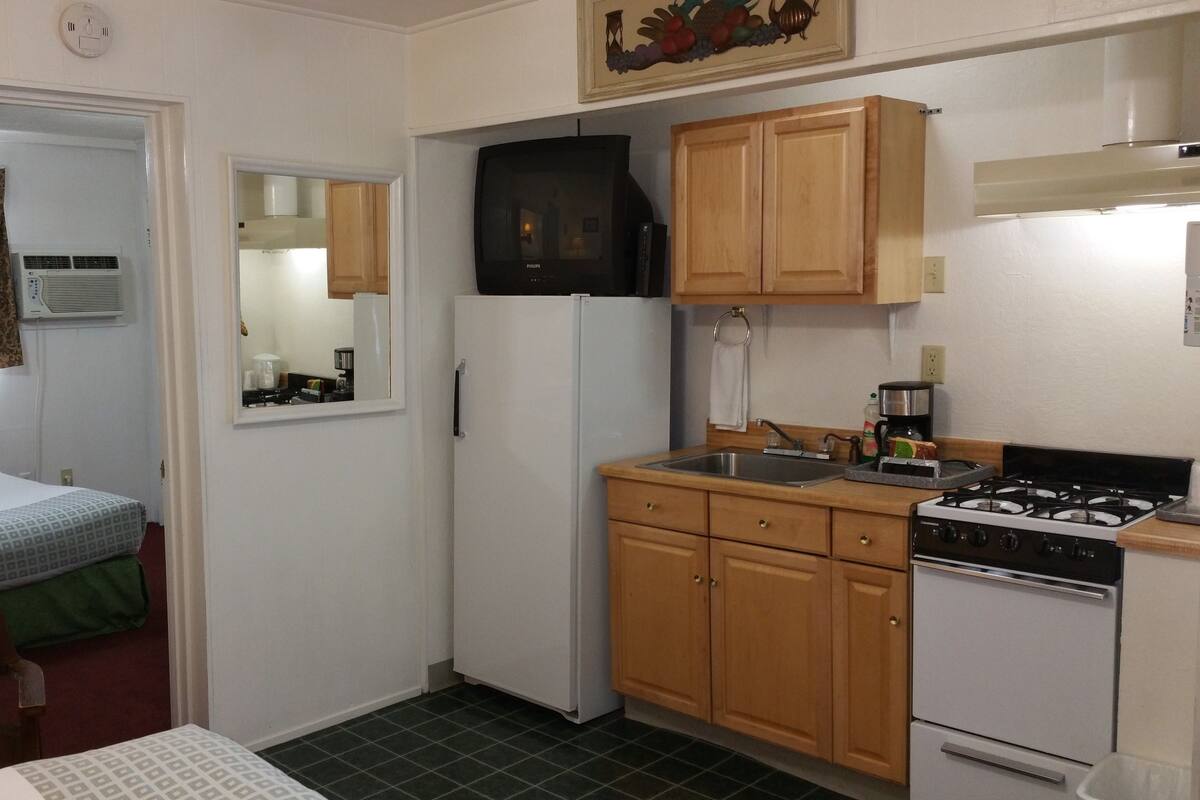 A compact kitchen with a refrigerator, stove, and wooden cabinets.