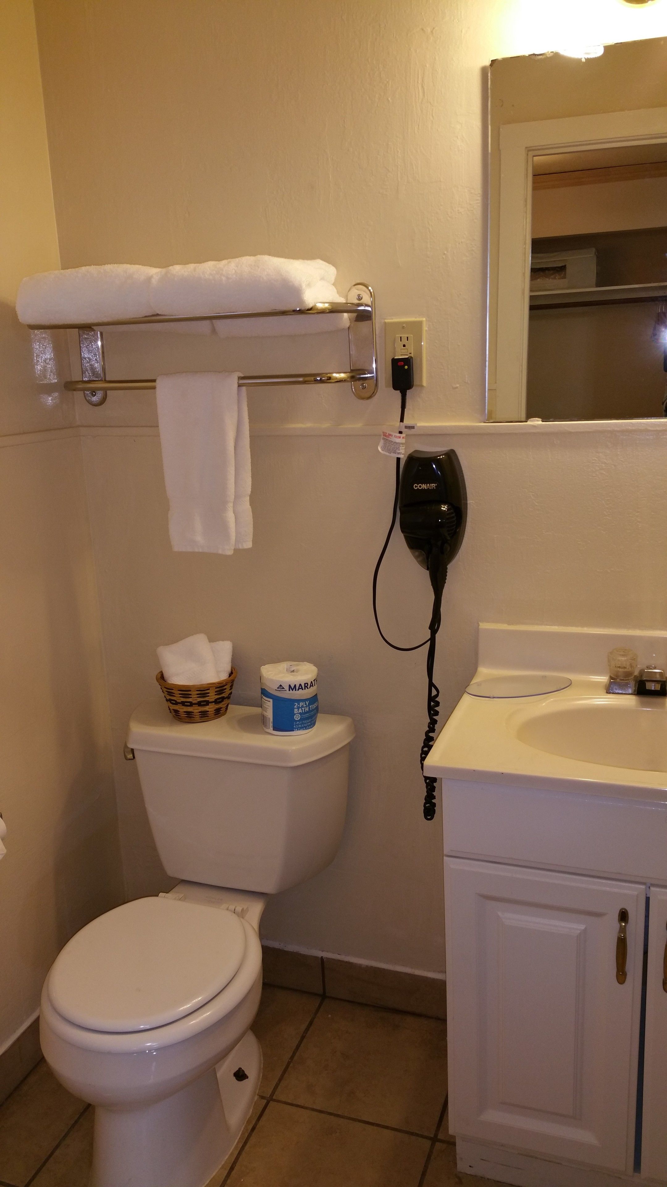Une salle de bain équipée de toilettes, d’un panier rempli de serviettes, d’un sèche-cheveux et d’un paquet de mouchoirs.