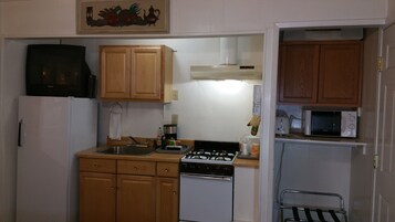 Cocina compacta con armarios de madera, cocina a gas, lavavajillas, microondas y refrigerador.