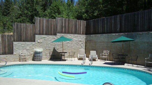 A swimming pool with a stone wall, lounge chairs, and umbrellas. - El Dorado Motel (Twain Harte)