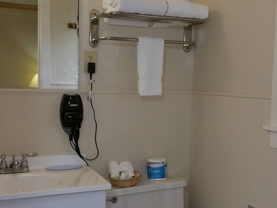 A bathroom with a white sink, a mirror, a towel rack with towels, a toilet, and a toilet paper holder.