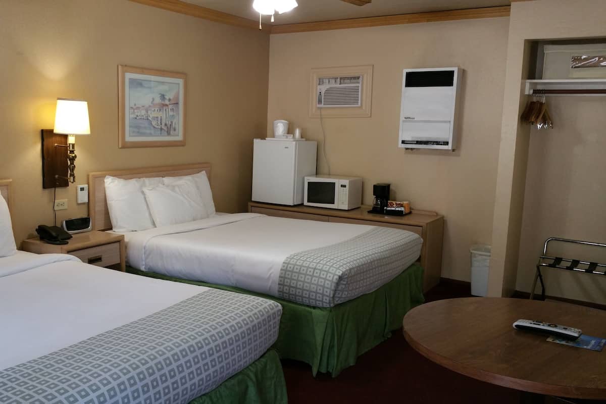 A hotel room with two beds, a desk with a microwave, a coffee maker, and a TV.