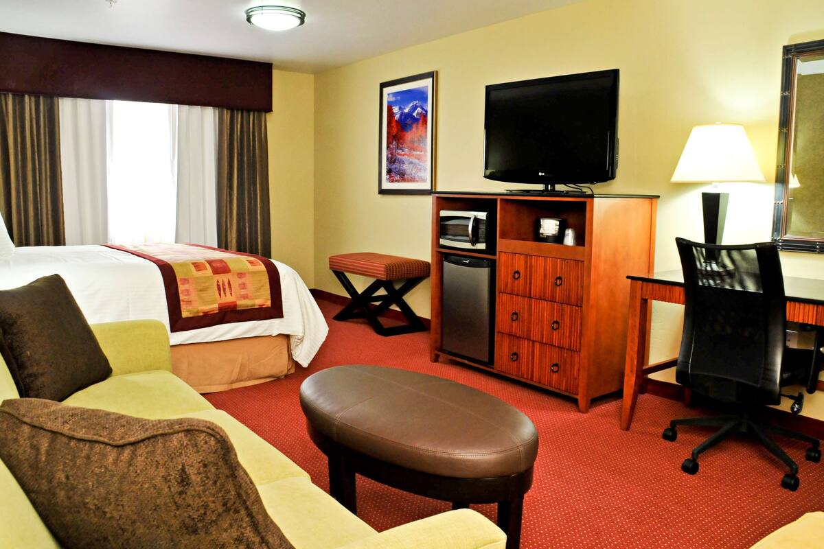 A hotel room with a bed, a desk, a television, a microwave, and a chair.