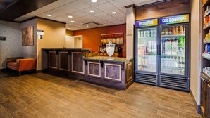 Un hall d’hôtel comprenant un comptoir d’accueil, une machine à café et un présentoir réfrigéré pour les boissons.