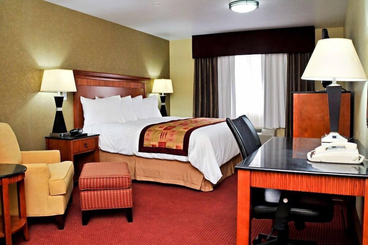 A hotel room with a bed, two bedside tables with lamps, a desk with a telephone, a chair, and an ottoman.