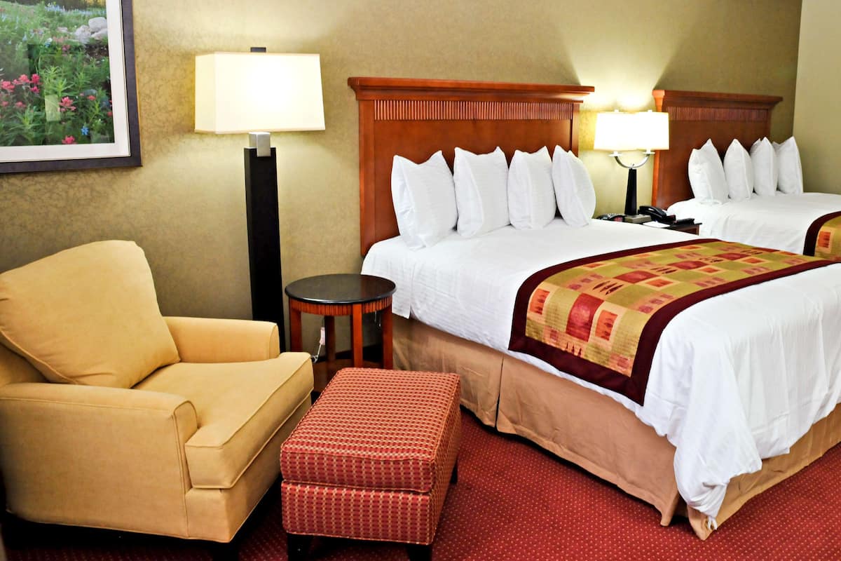 A hotel room with two beds, a sofa, a small round table, and a lamp.