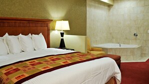 Une chambre d’hôtel avec un grand lit, une table de chevet avec une lampe, une salle de bain avec une baignoire et une moquette rouge.