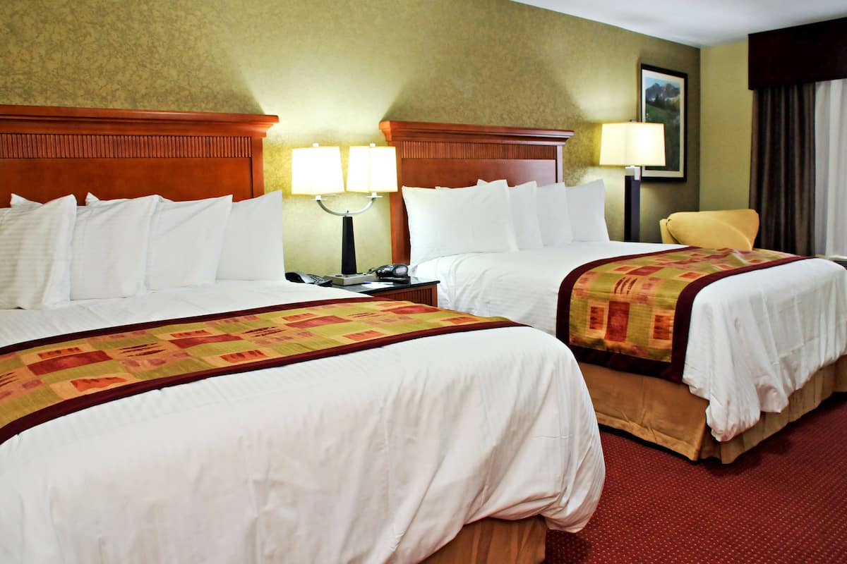 A hotel room with two beds, a nightstand with a lamp, and a chair.