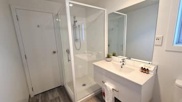 A modern bathroom with a glass-enclosed shower, a white vanity with a mirror, and a towel rack.