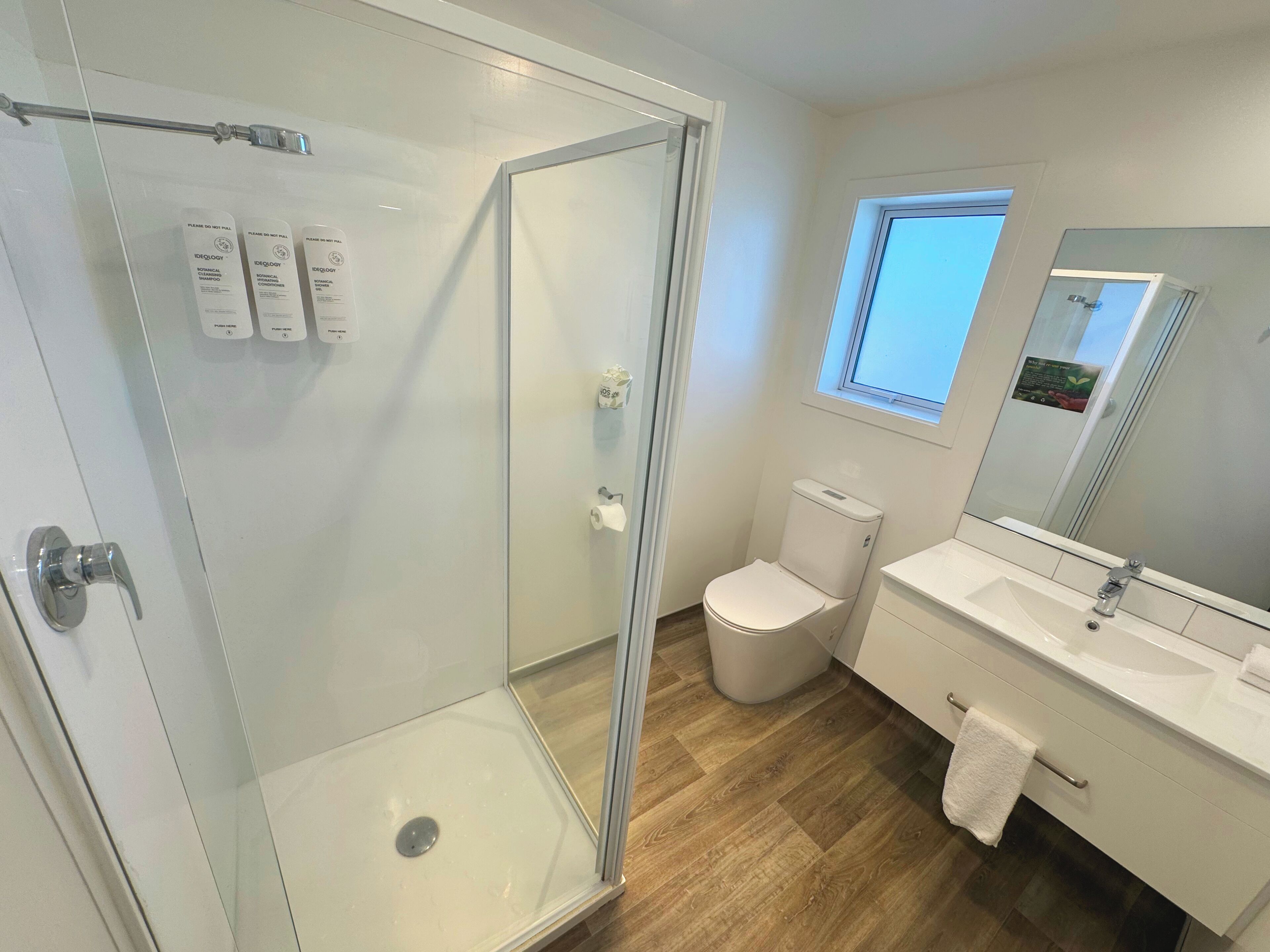 A modern bathroom with a glass shower enclosure, a toilet, and a sink with a mirror above it.