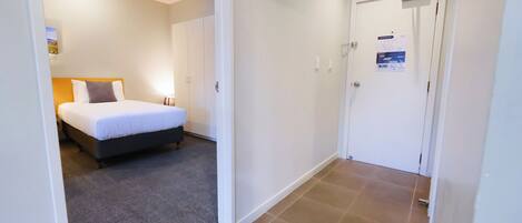 A hotel room with a bed, a carpeted floor, a white door, and a light switch on the wall.