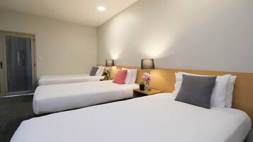 Habitación de hotel con dos camas individuales, cabecero de madera, lámparas de noche y una mesita con un jarrón de flores.