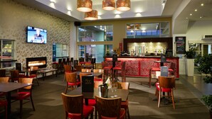A restaurant with multiple tables and chairs, a bar area, and a television mounted on the wall. - Garden Hotel Christchurch (Christchurch)