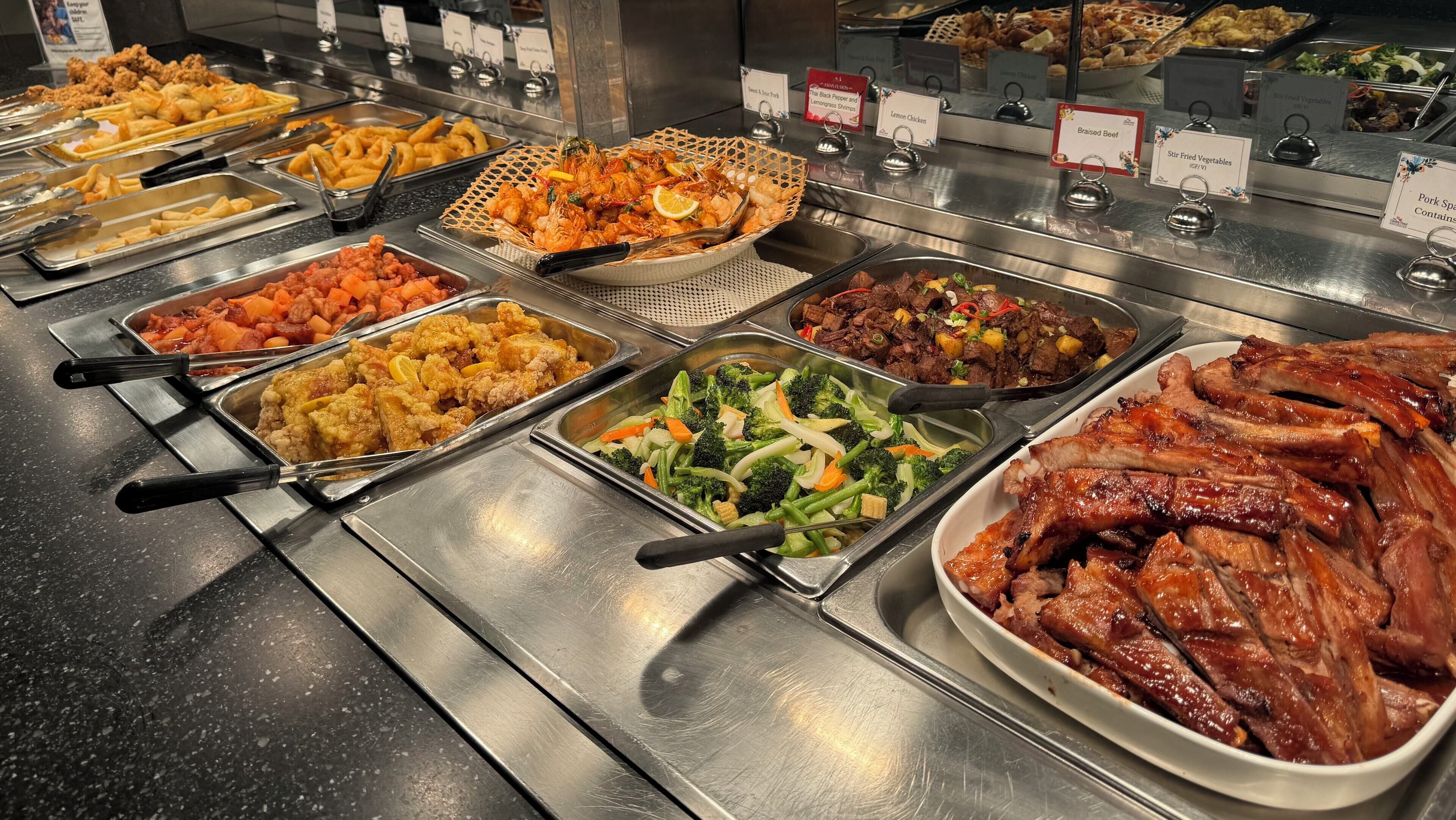 Un buffet proposant divers plats, notamment du poulet frit, des crevettes, des légumes sautés et du bœuf braisé.