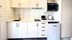 A compact kitchen with white cabinets, a sink, a microwave, and a coffee maker. - Garden Hotel Christchurch (Christchurch)