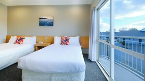 A hotel room with two beds, a nightstand, a painting on the wall, and a large window with a view of the sky and buildings. - Garden Hotel Christchurch (Christchurch)