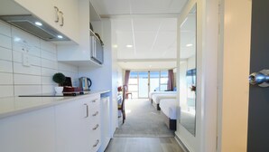 A modern hotel room with a kitchenette, a large window with curtains, and a view of the outside. - Garden Hotel Christchurch (Christchurch)