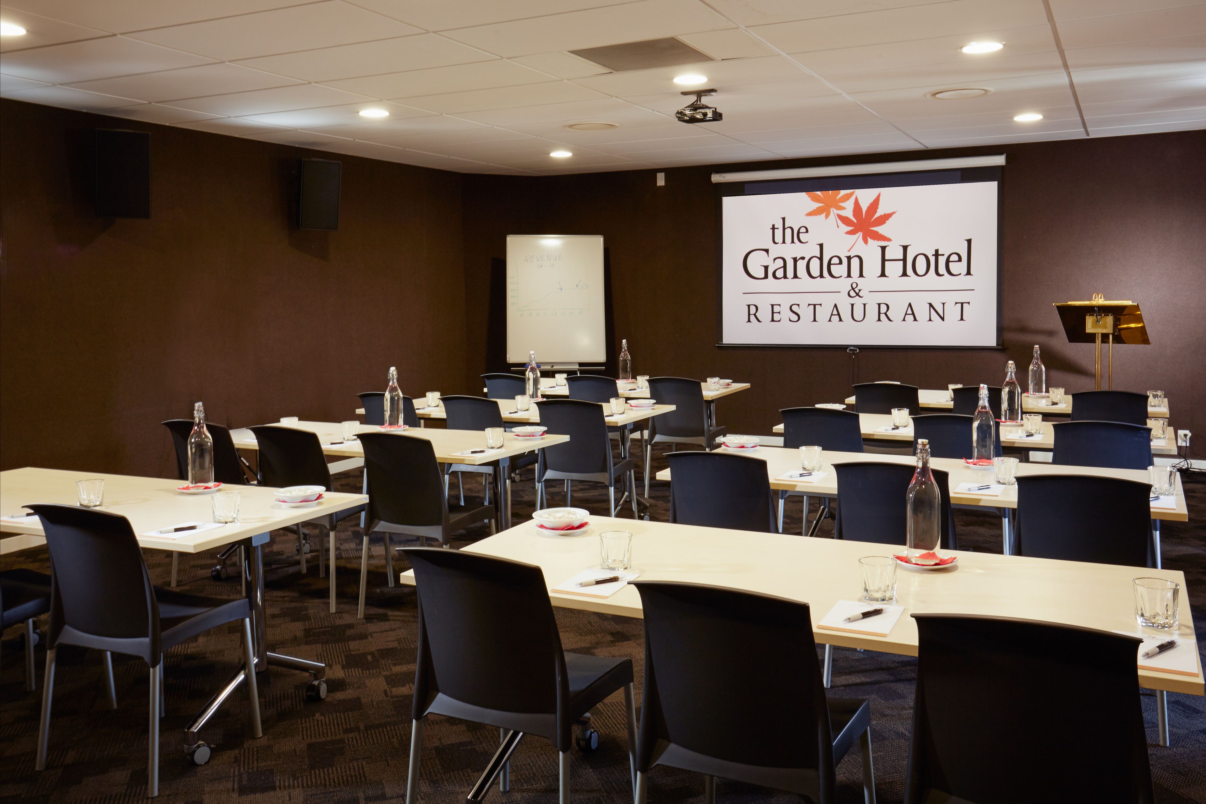 A conference room at the Garden Hotel & Restaurant with multiple tables and chairs, a whiteboard, and a projector screen.