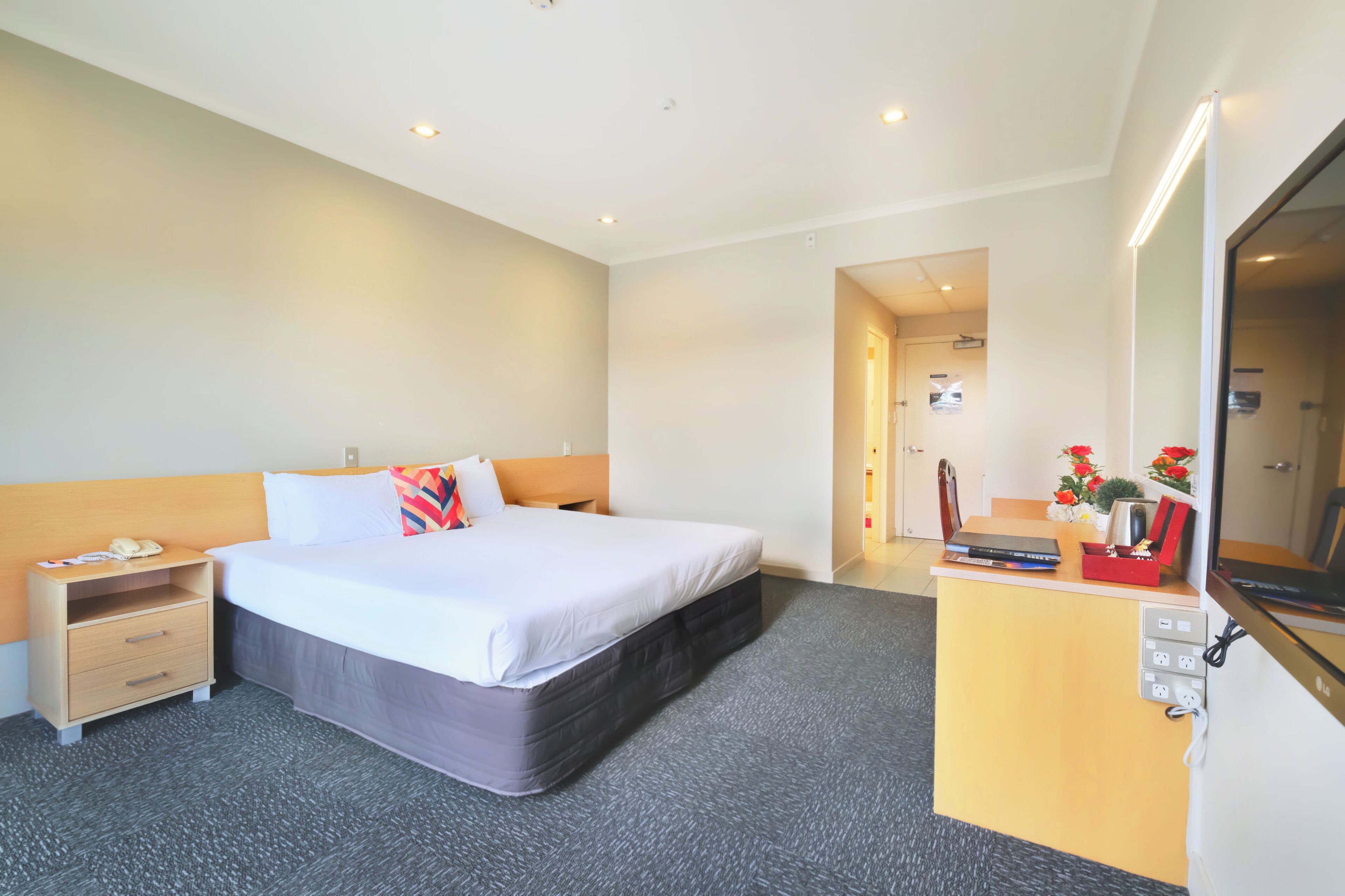 Een hotelkamer met een bed, nachtkastje, bureau en een spiegel.