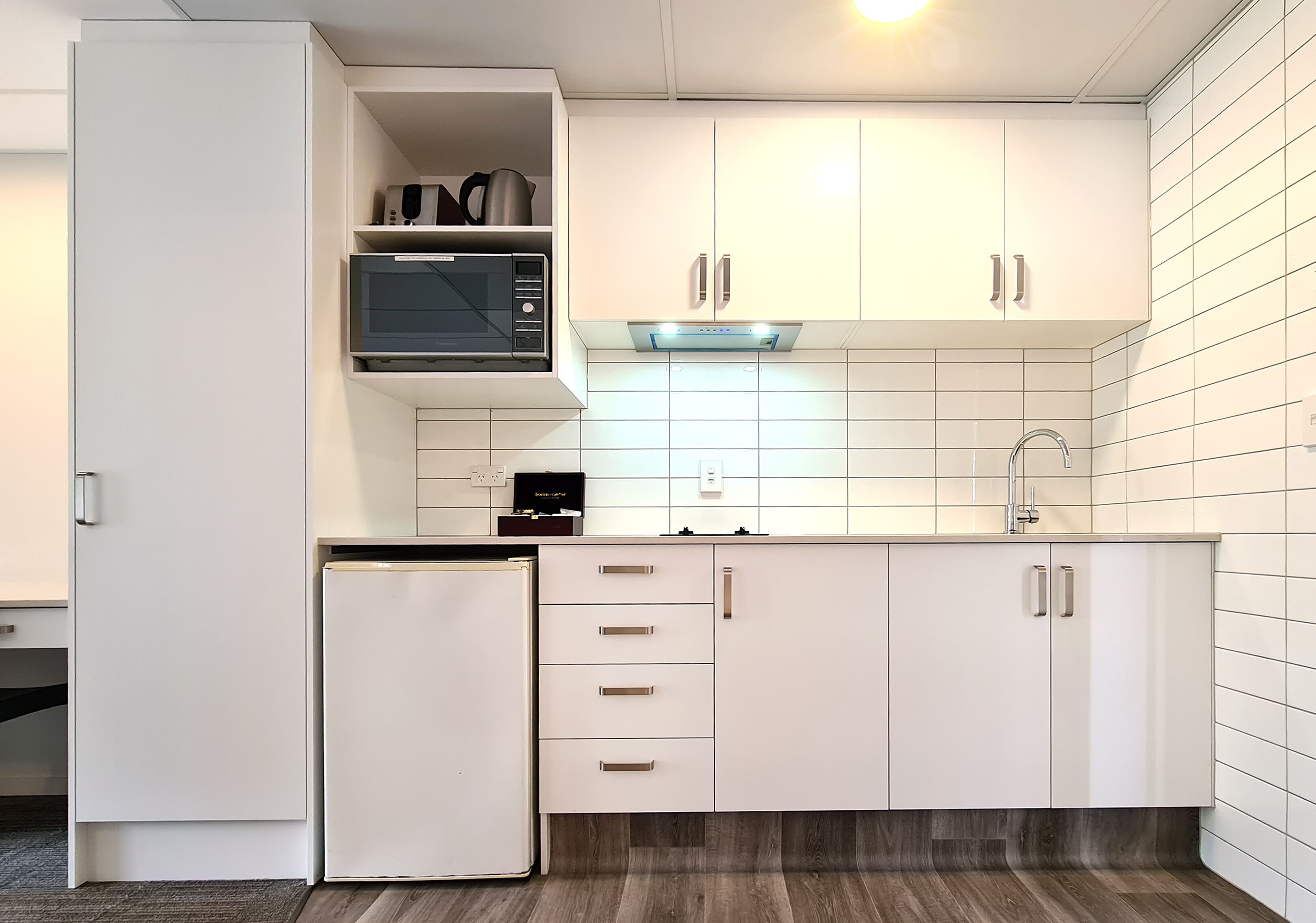 A modern kitchen with white cabinets, a built-in microwave, and a stainless steel range hood.