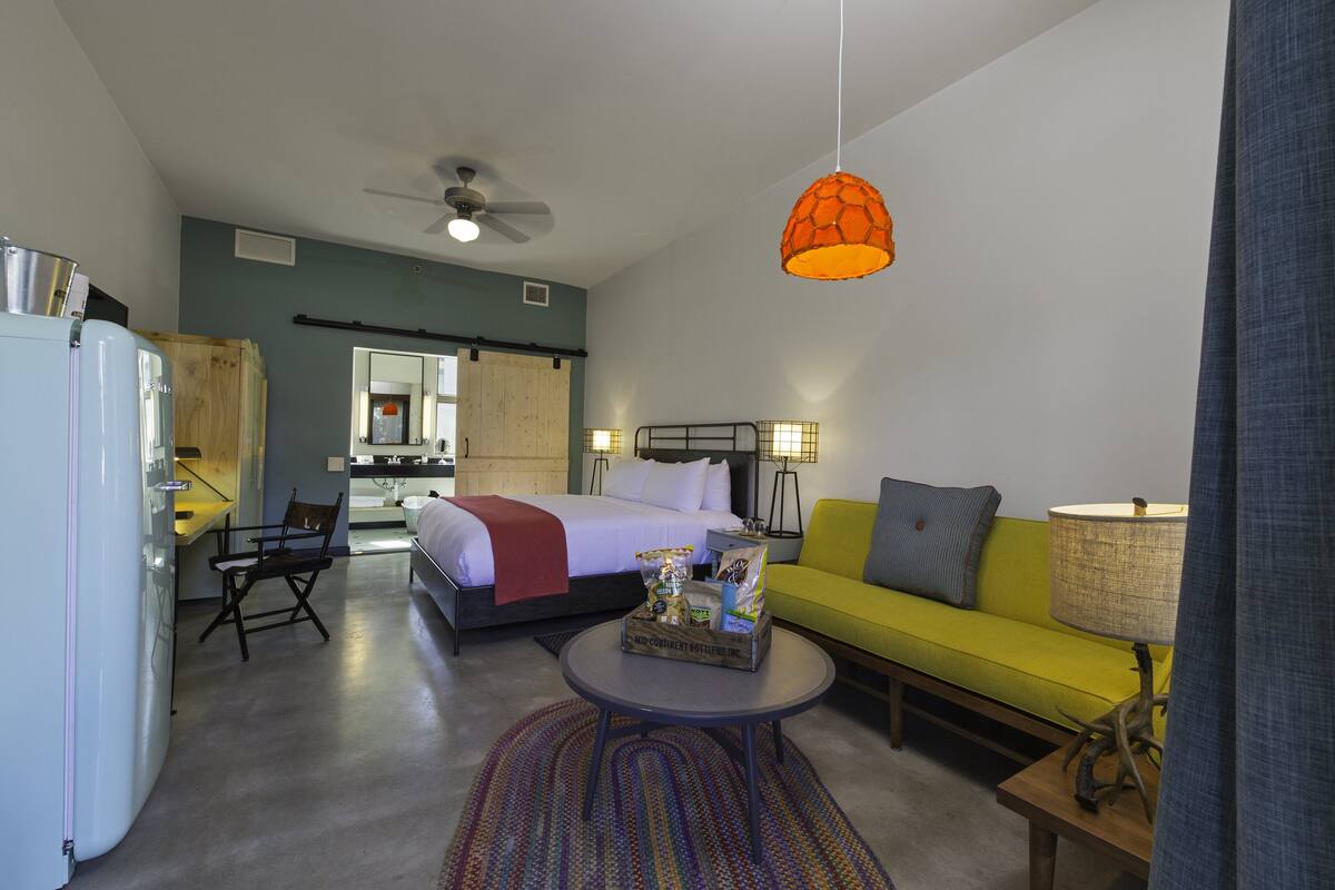 A compact hotel room with a bed, a sofa, a dining area, and a kitchenette.