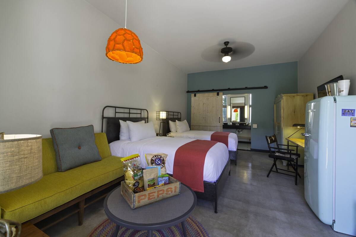 A hotel room with two beds, a sofa, a dining table, and a refrigerator.