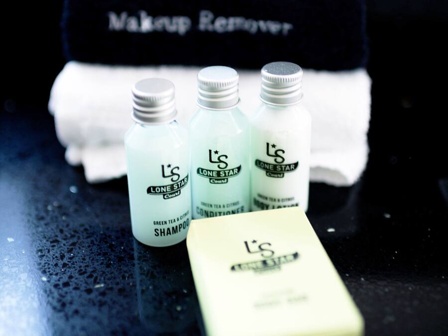 Tres botellas de champú y acondicionador L'S Lone Star, una pastilla de jabón blanca y una toalla negra con la inscripción 'Makeup Remover'.