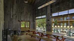 A rustic wooden interior with large windows, a picnic table, and outdoor seating visible through the windows. - Lone Star Court, by Valencia Hotel Collection (Austin)