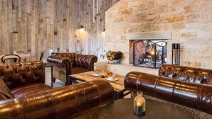 A rustic interior with leather seating, a stone wall, and a fireplace. - Lone Star Court, by Valencia Hotel Collection (Austin)