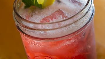 A glass jar with a red beverage, ice cubes, and a lemon slice with mint leaves.
