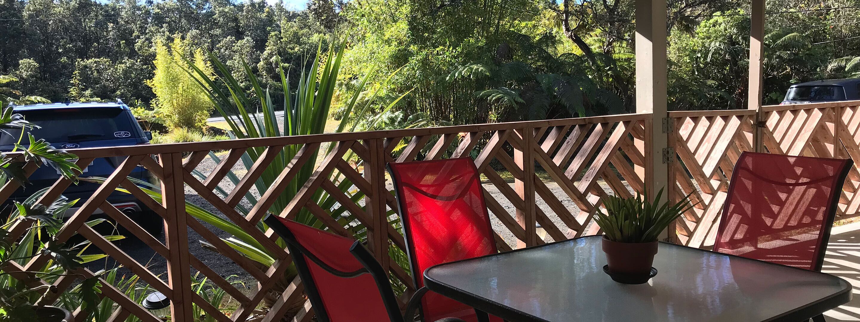 Ein Balkon mit Holzlattenzaun, einem Tisch und zwei roten Stühlen.