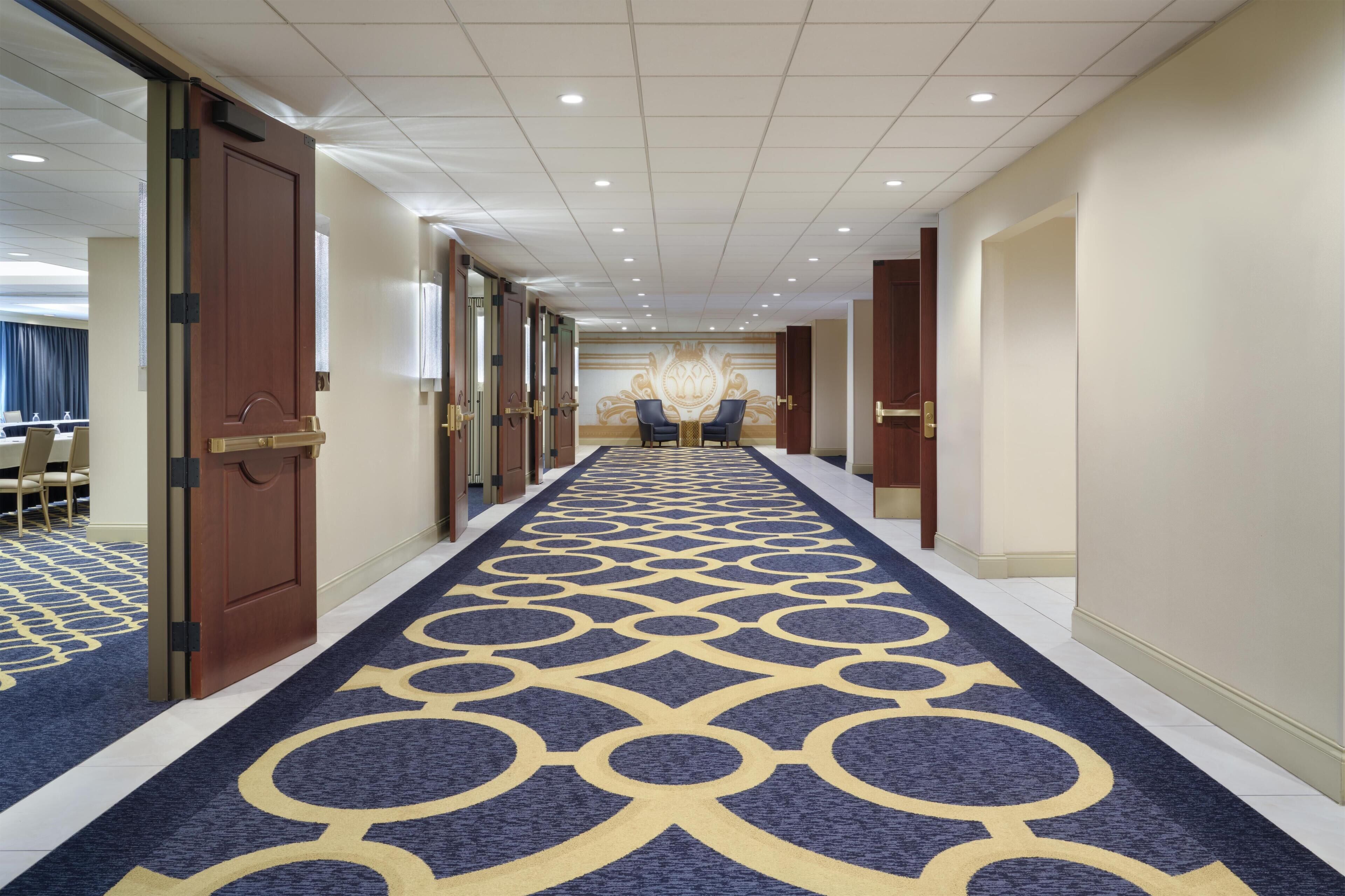 A hotel corridor with a patterned carpet, doors, and a mirrored wall.