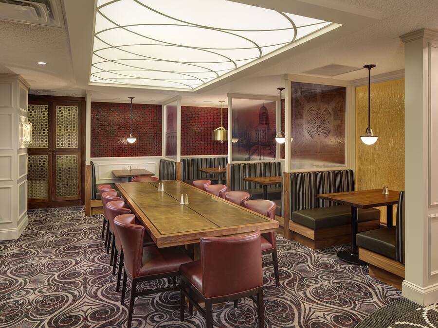 A dining area with a long wooden table, multiple booths, and patterned carpet.