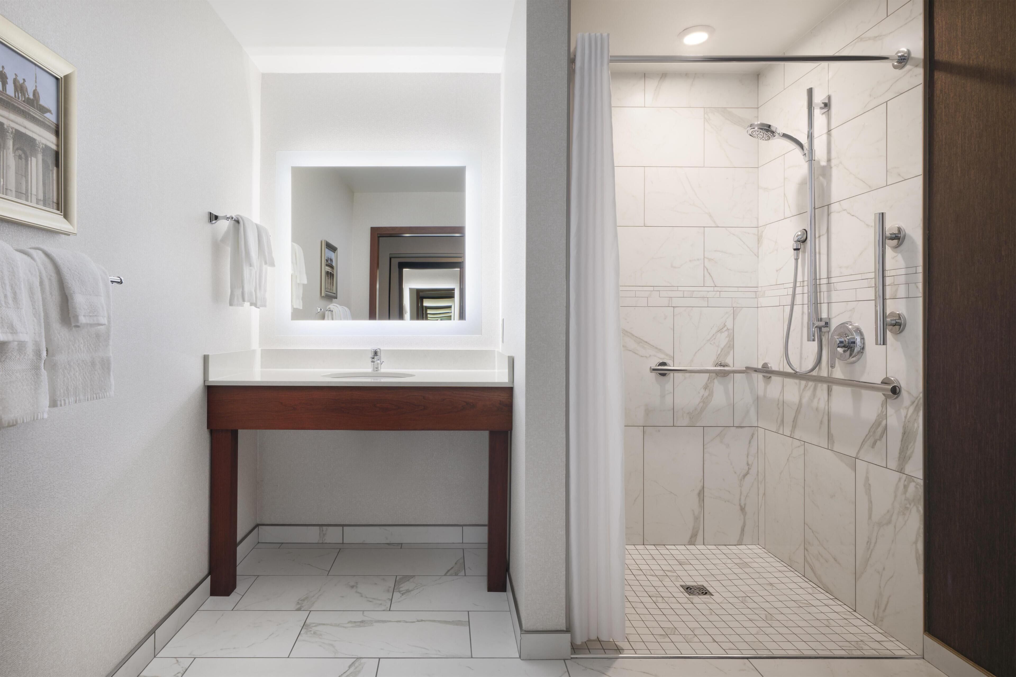 Un baño con ducha de mármol, tocador de madera y un espejo grande.