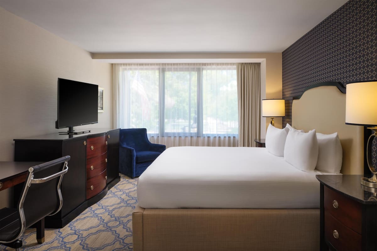 A hotel room with a bed, a desk with a TV, a chair, a dresser, and a window with curtains.