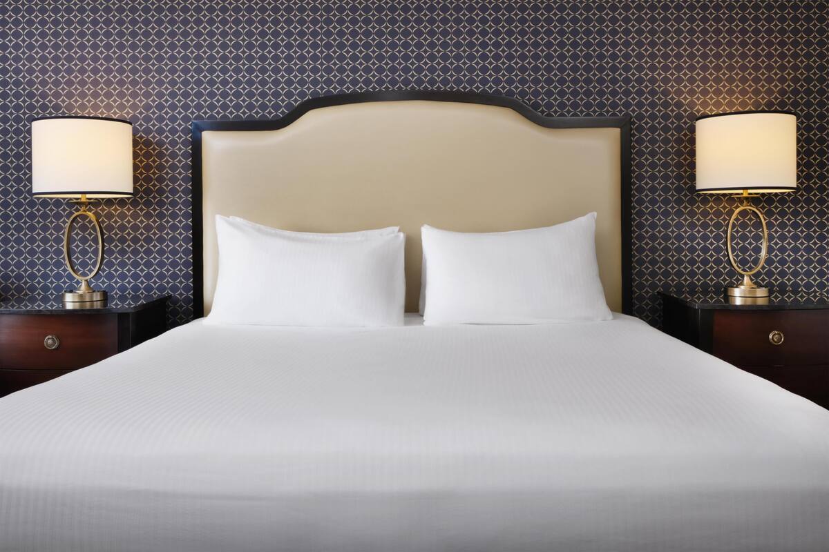 Un lit avec une tête de lit, deux tables de chevet avec des lampes et un mur décoré d’un motif.