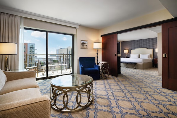 A hotel room with a balcony, a bed, a blue armchair, a round glass table, and a patterned carpet.