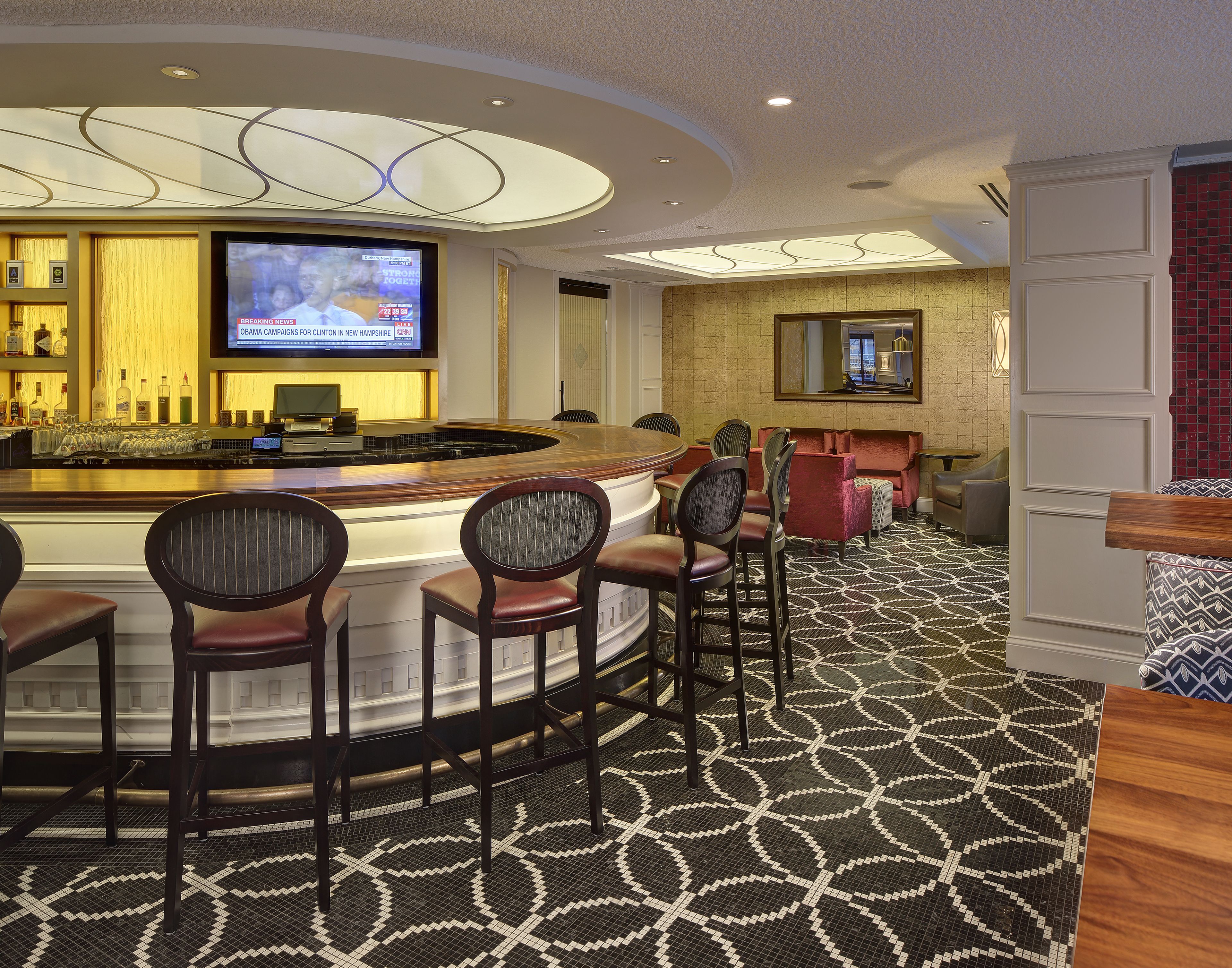 A bar area with a TV displaying news, bar stools, and a patterned floor.