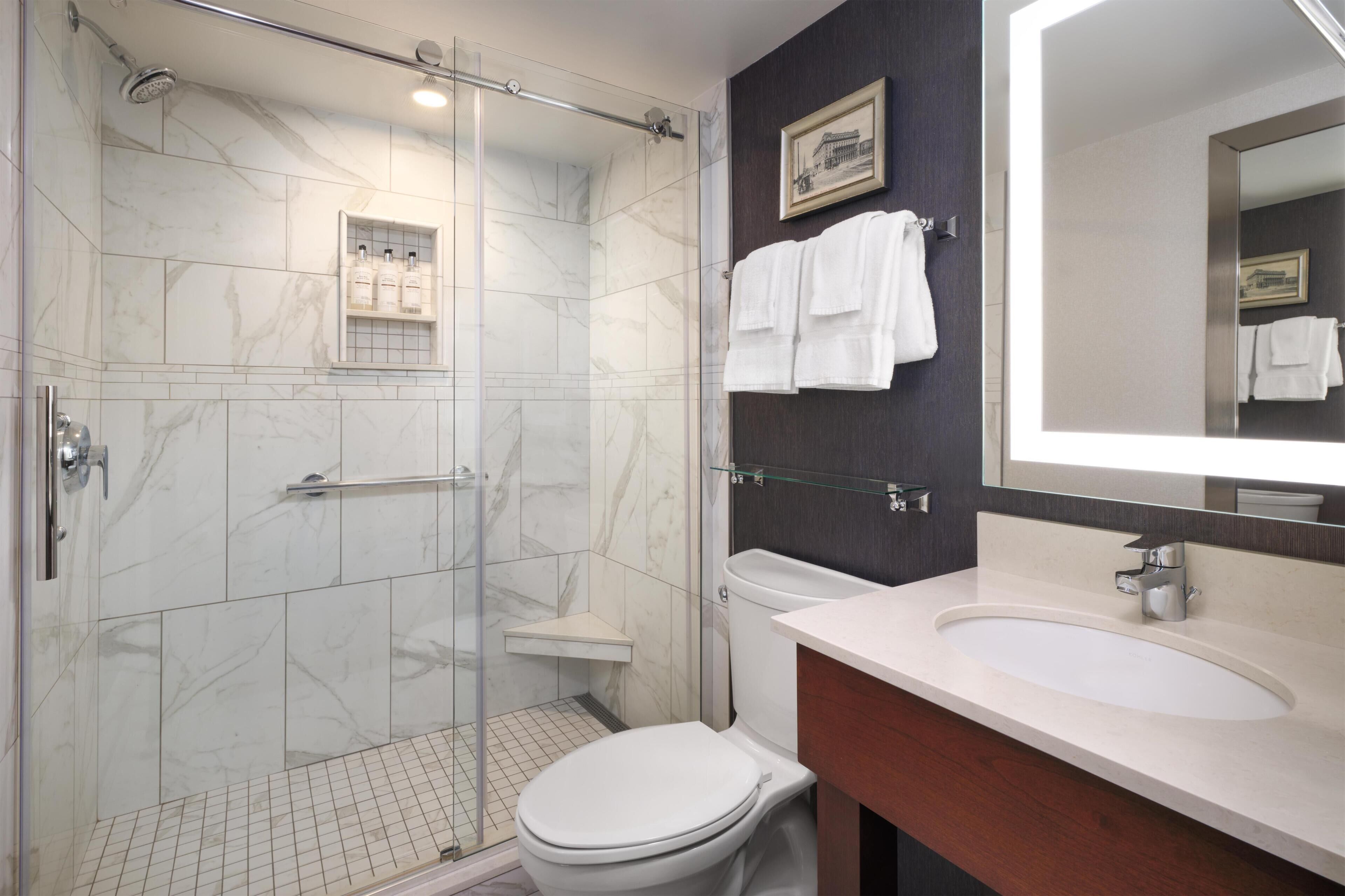 A bathroom with a glass-enclosed shower, a white toilet, a vanity with a sink, and a mirror.