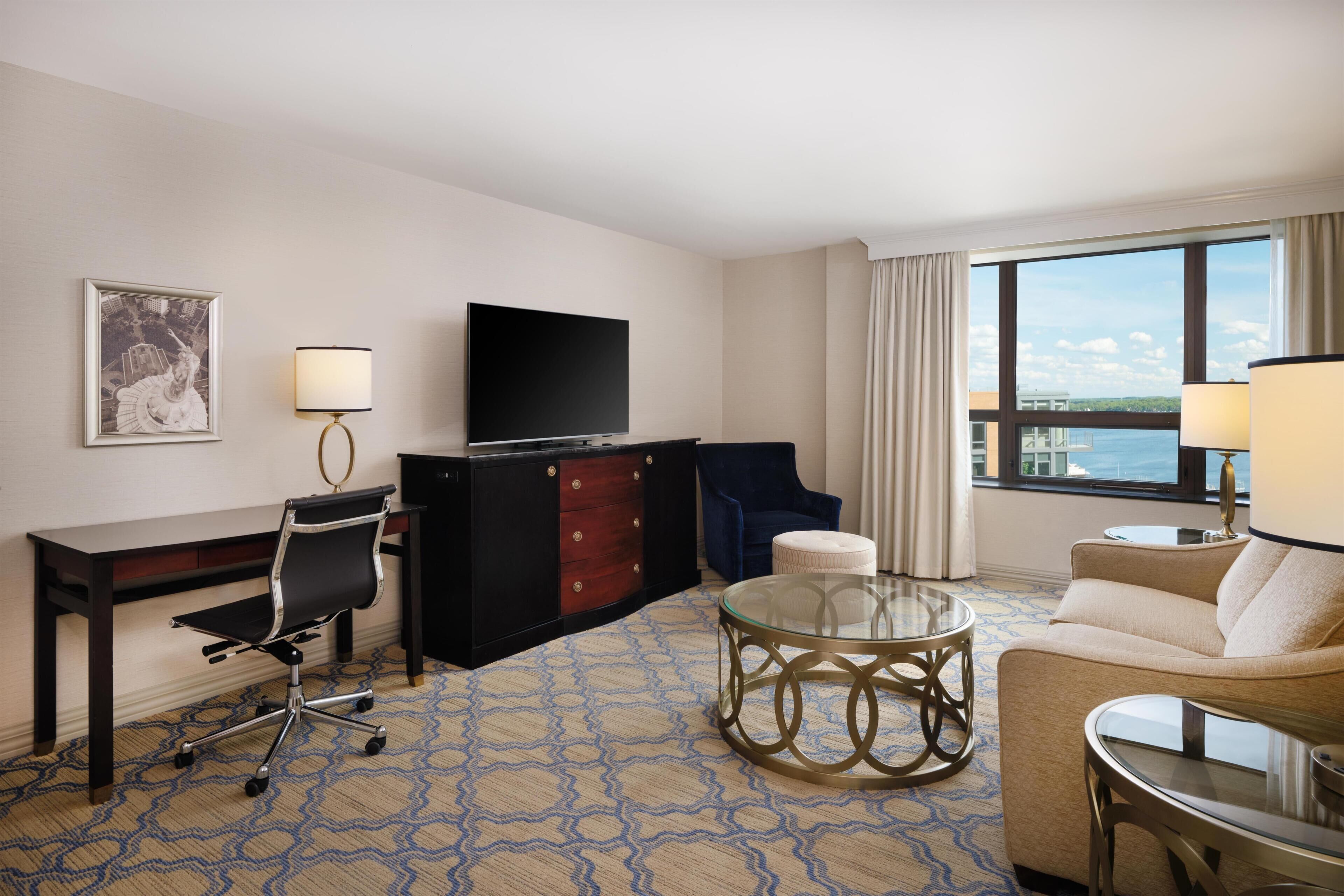 Habitación de hotel con escritorio, televisor, sofá y vista al mar.