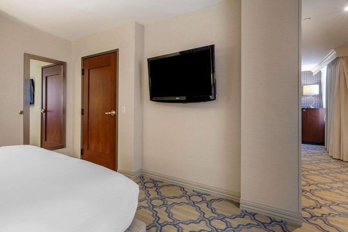 Une chambre d’hôtel avec un lit, un téléviseur fixé au mur et une moquette à motifs.