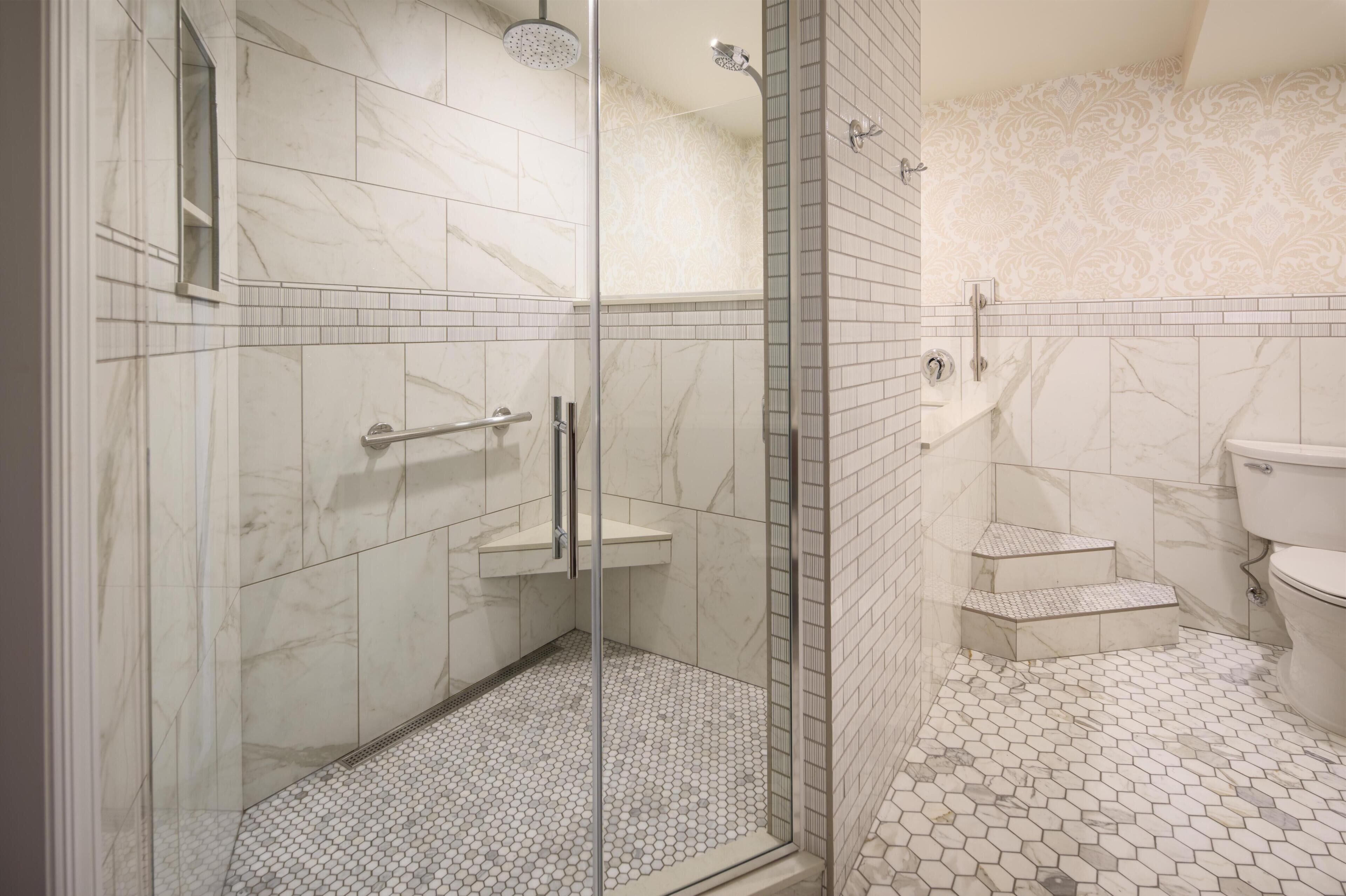 Un baño moderno con ducha de vidrio, piso de mármol y un inodoro con diseño elevado.